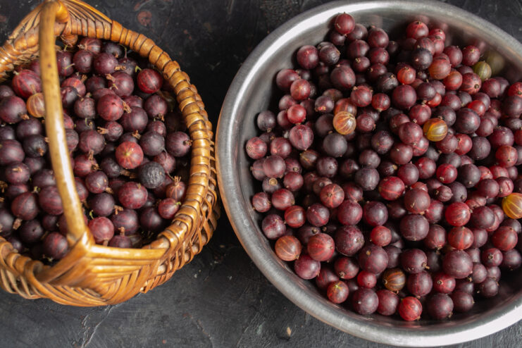 A bowl of fresh red gooseberries being prepared, with tops and tails removed.