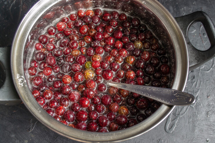 Red gooseberries being added to a pot of boiling sugar syrup.