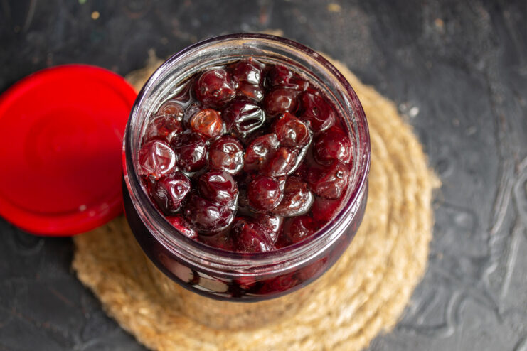 Hot red gooseberry jam being poured into a sterile glass jar for preservation.