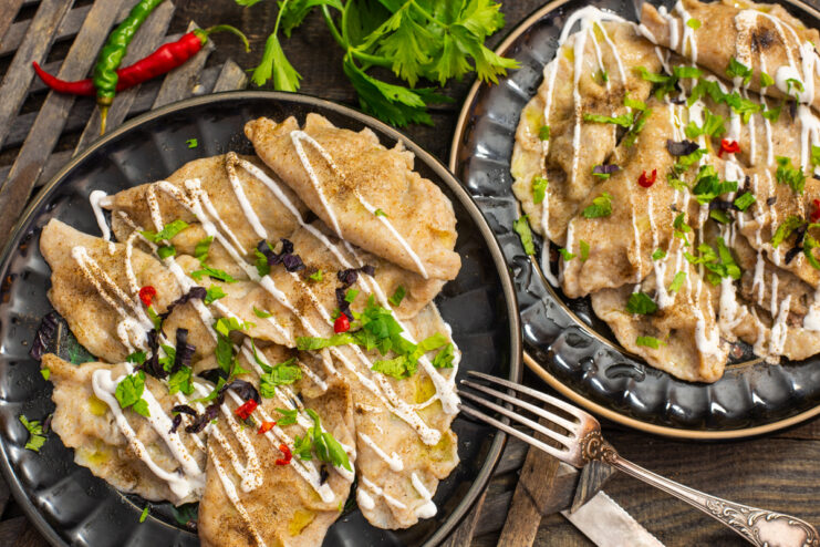 A white bowl filled with cooked vareniki with meat, garnished with fresh herbs and chili.