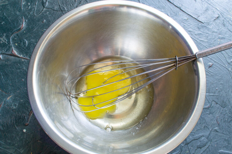 Step 1: Starting the Vareniki Dough with an Egg A chicken egg being cracked into a glass bowl with a whisk inside.
