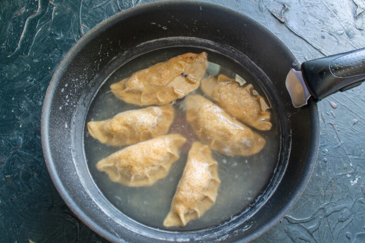 Cooking the Vareniki: Boiling Until They Float Several uncooked vareniki being dropped into a pot of boiling water.