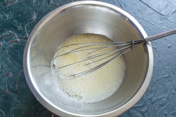 Mixing Wet Ingredients: Adding Cold Milk to the Dough Cold milk being poured into the egg and oil mixture in a glass bowl.