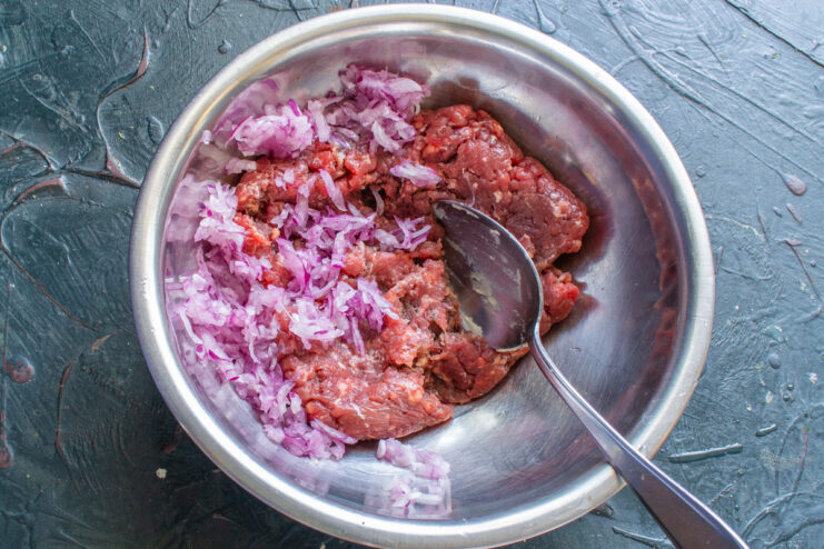 Preparing the Filling: Grating Red Onion for Flavor A red onion being grated on a box grater for the meat filling.