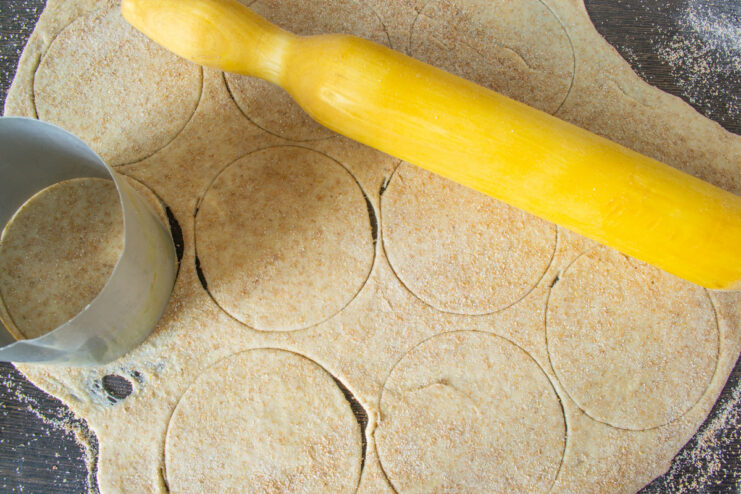 Rolling Out the Whole Wheat Dough for Vareniki A ball of dough being rolled out with a rolling pin on a floured wooden board.