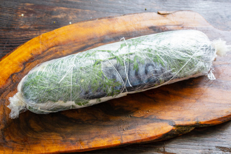 Step 6: Securing the Mackerel Roll with String for a Perfect Shape The plastic-wrapped mackerel roll being tied with kitchen twine.