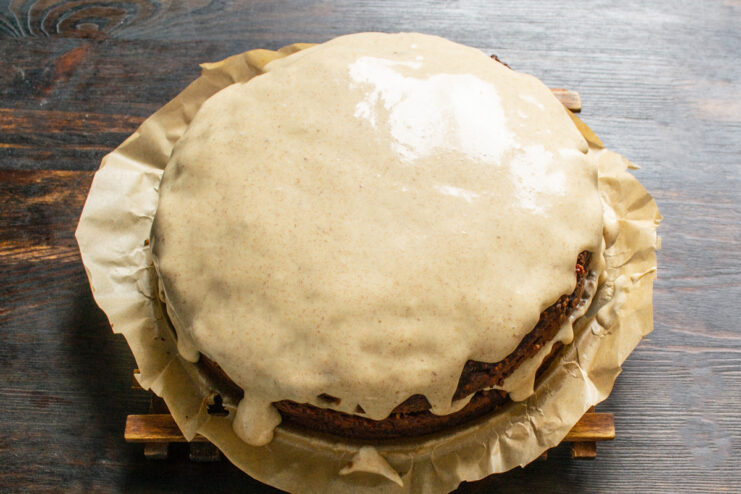 The final layer of creamy frosting being poured over the assembled chocolate ginger cake.