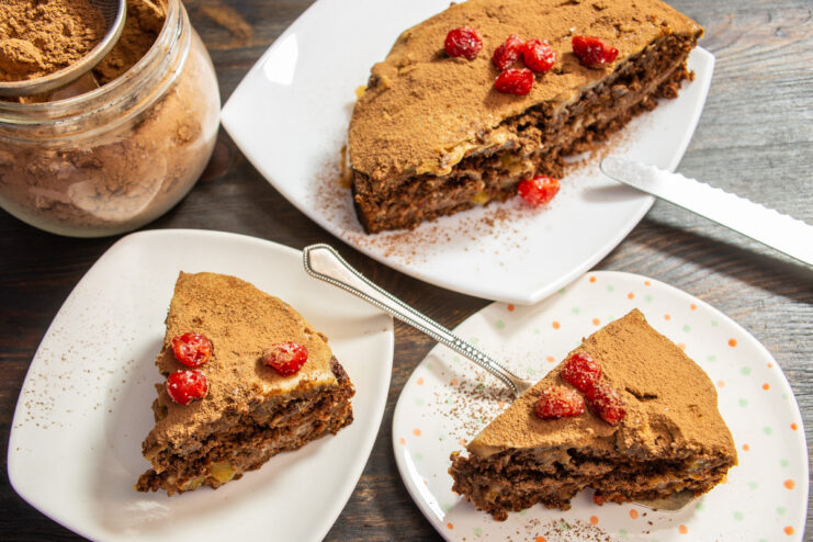 The finished vegetarian chocolate ginger cake being decorated with a dusting of cocoa powder and candied cherries.