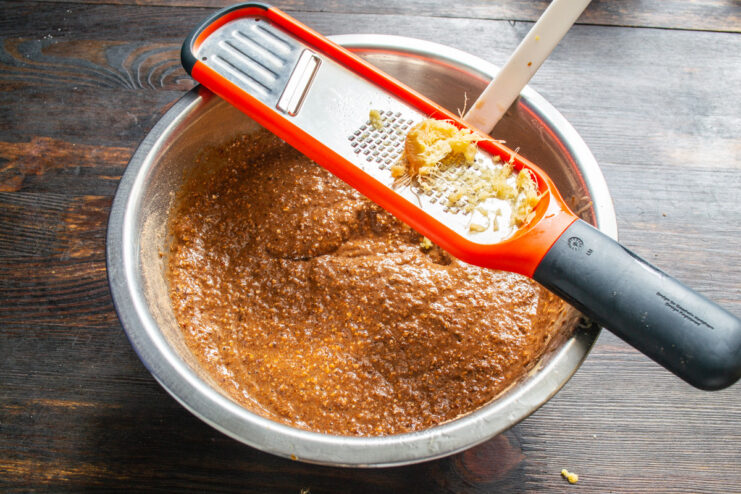 Freshly grated ginger root being added to the chocolate cake batter in a bowl.