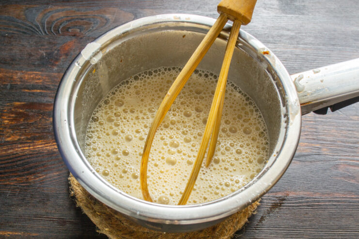 A hand whisking a creamy mixture in a saucepan to make the frosting for the cake.