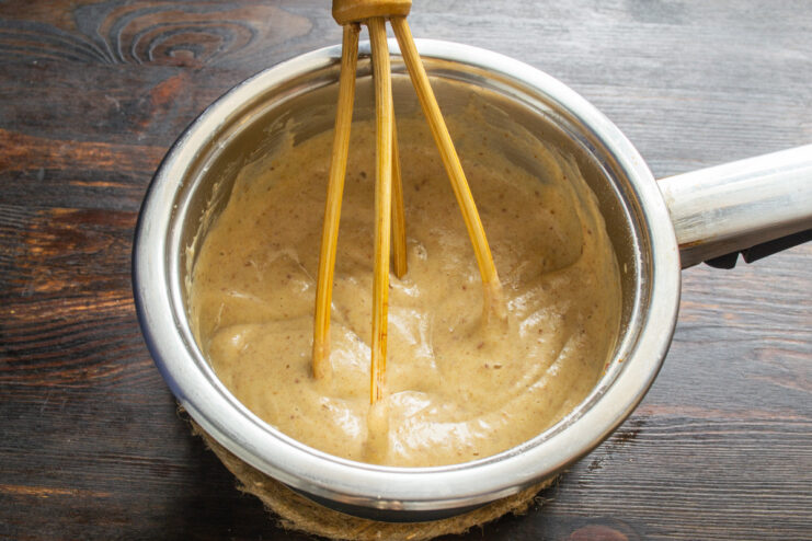 A saucepan on a stove with a creamy frosting being stirred as it thickens.