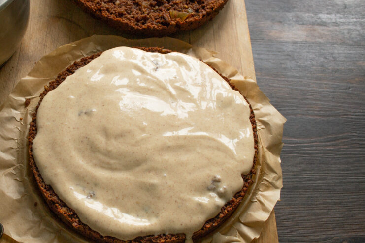A layer of chocolate ginger cake being generously covered with creamy white frosting.