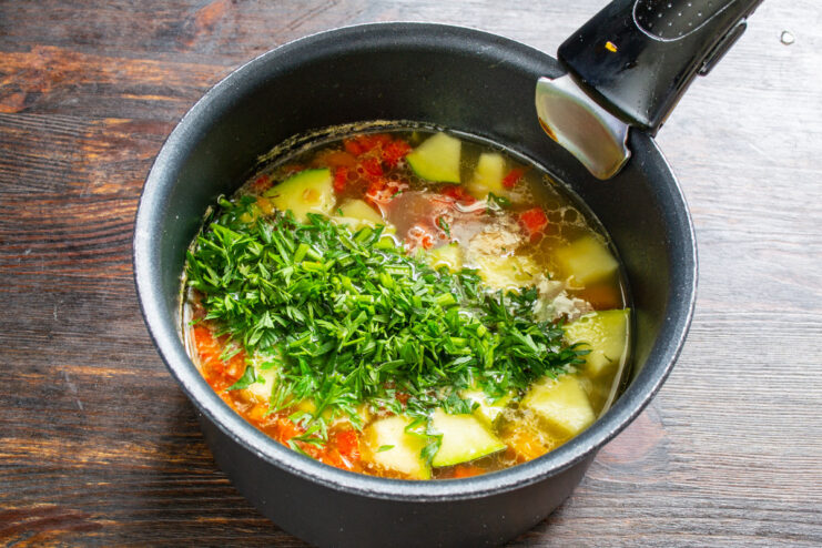 Adding nutritious carrot tops for extra greens Finely chopped carrot tops being added to the simmering vegetable soup.