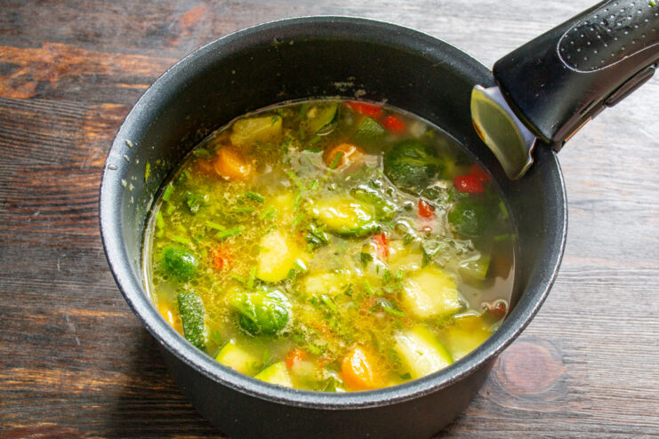 Seasoning the soup to enhance all the vegetable flavors Adding a spoonful of spices to the vegetarian soup in the pot.
