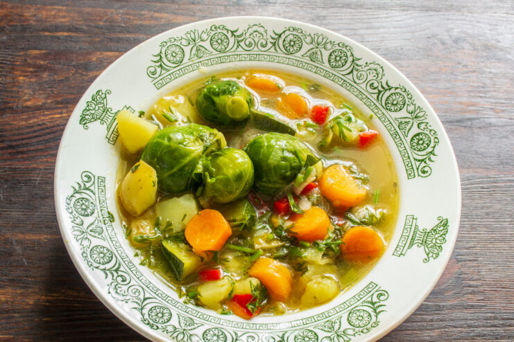 Serving the finished vegetarian soup A ladle serving the hot vegetarian soup with Brussels sprouts and zucchini into a bowl.