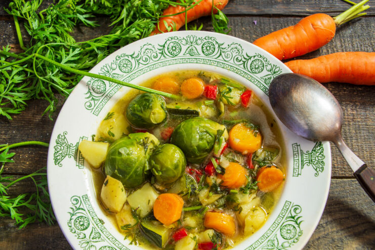 A white bowl filled with vegetarian soup containing Brussels sprouts, zucchini, and carrots.