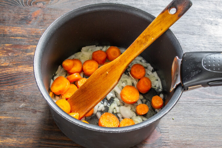 Adding fresh carrots to the aromatic base Sliced carrots being added to the pot with sautéed onions and garlic.