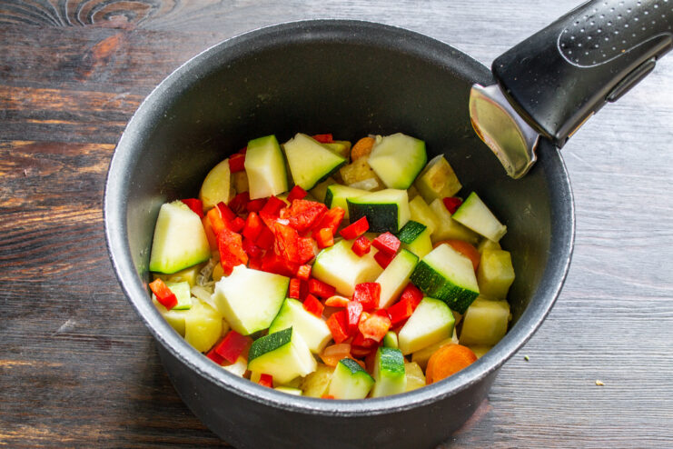 Adding colorful bell pepper for sweetness and flavor Diced red bell pepper is added to the mix of vegetables in the pot.