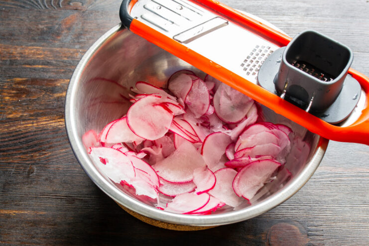 Perfectly Thin Radish Slices for a Crisp Salad A close-up of red radishes being thinly sliced on a cutting board.