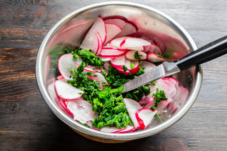 Combining Fresh Radishes and Prepared Nettles A bowl of sliced radishes with a pile of chopped blanched nettles being added.