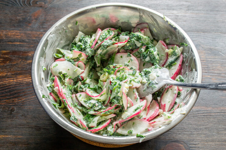 Tossing the Spring Salad to Combine All Flavors Mixing the radish, nettle, egg, and green onion salad with a creamy dressing in a bowl.