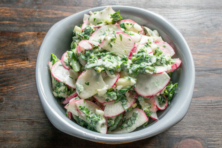 Serving the Delicious and Healthy Nettle and Radish Salad The finished spring salad with red radish and nettle being served in a white salad bowl.