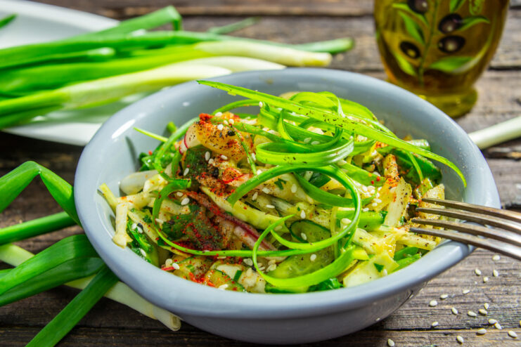 A bowl of freshly made spring green onion salad, garnished with curled onions and sesame seeds.