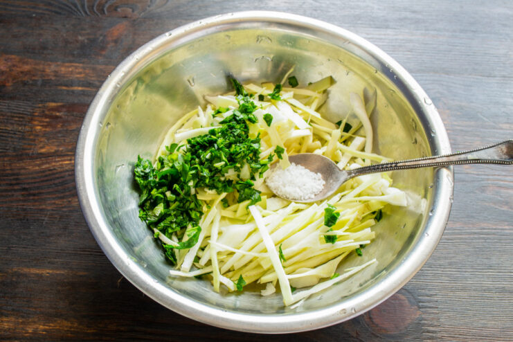 How to prepare cabbage for salad: massaging with salt Hands massaging shredded cabbage and herbs with salt in a glass bowl.