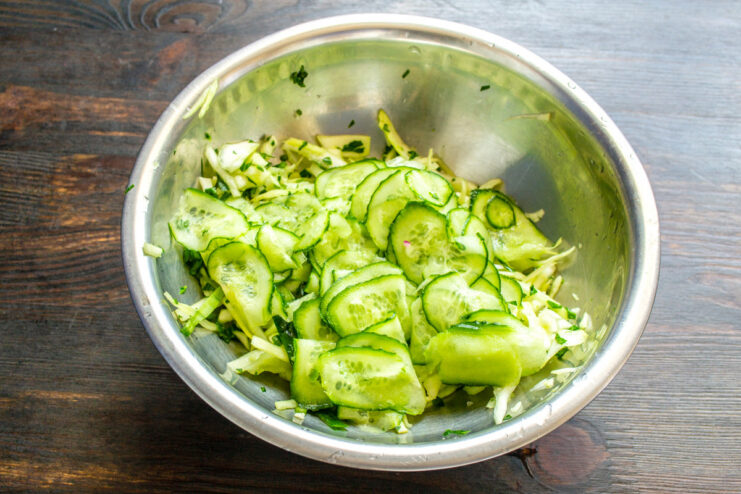 Preparing cucumbers for the spring salad A hand slicing a fresh cucumber into thin slices on a cutting board.