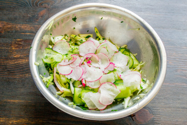 Combining the main salad ingredients Sliced red radishes being added to a bowl of cabbage and cucumbers.