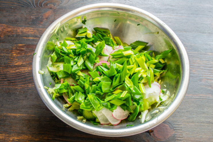 Adding fresh green onions to the salad mix Chopped green onions being added to the vegetable salad in a bowl.