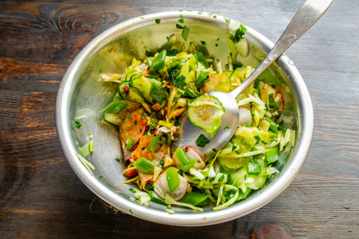 Dressing the spring salad for maximum flavor Pouring a lemon-oil dressing over the bowl of chopped vegetables.