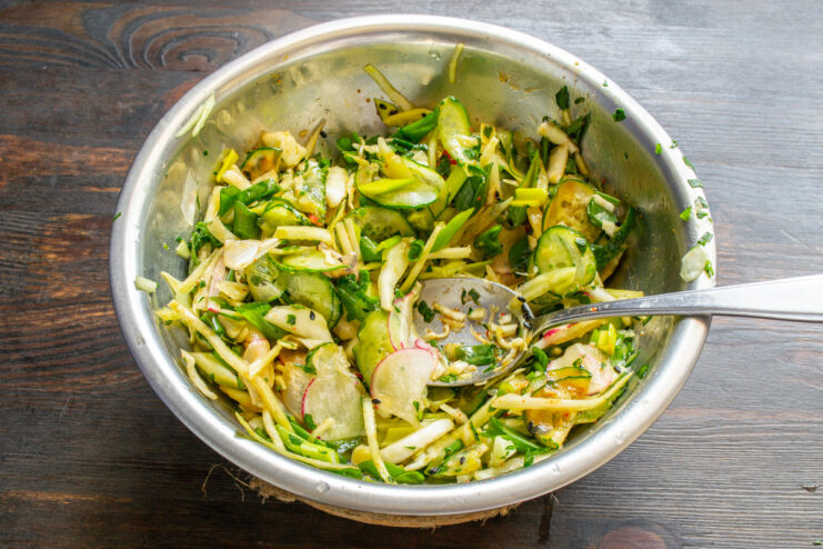 Tossing the salad to coat everything in dressing Tossing the spring salad with two spoons in a glass bowl to mix thoroughly.
