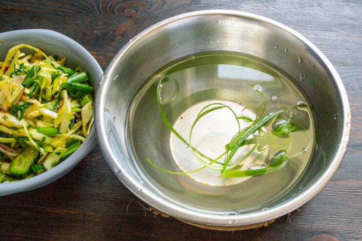 Creative garnish idea: curled green onions Thin strips of green onion being placed in ice water to create curls for garnish.