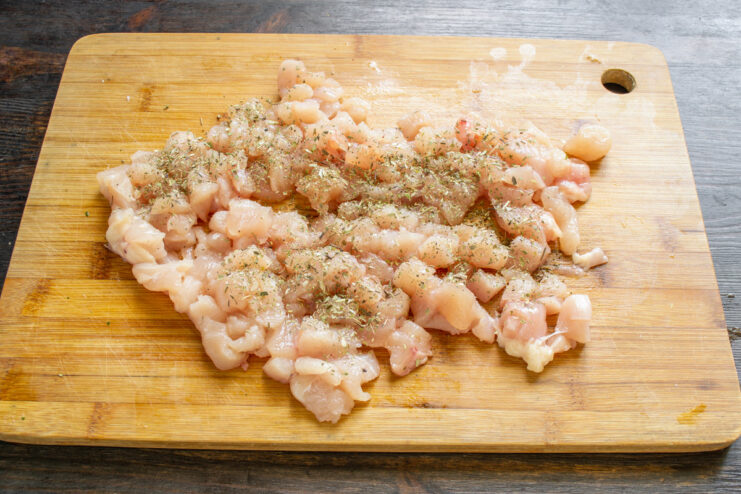 Step 2: Adding Spices to the Chicken Cubed chicken breast in a bowl being seasoned with dried herbs.