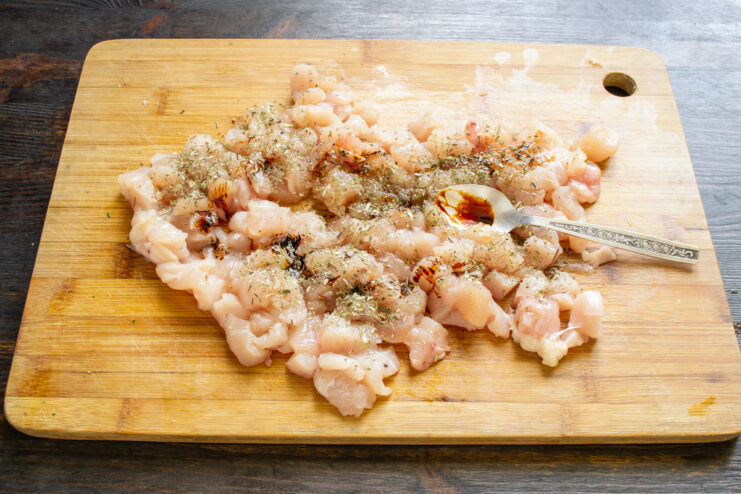 Step 3: Enhancing Flavor with Soy Sauce Soy sauce being poured over seasoned, cubed chicken breast in a bowl.