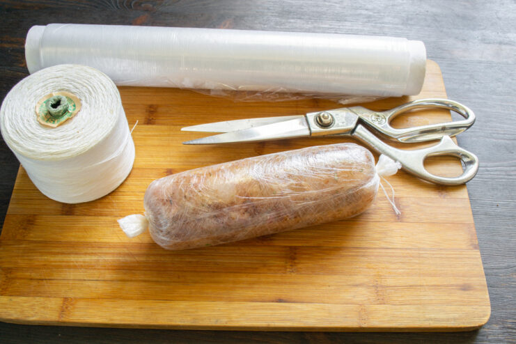Step 6: Shaping the Ham into a Log with Plastic Wrap The chicken mixture being formed into a tight log using plastic wrap.