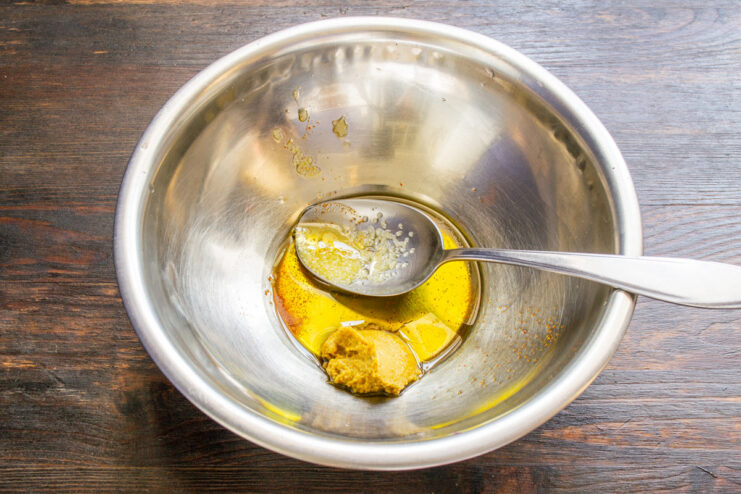 Preparing the Tangy Dressing for Vinegret Salad A close-up of a bowl with olive oil, mustard, salt, and pepper being mixed for the salad dressing.