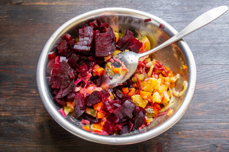 Adding the Star Ingredient: Beets! Diced cooked beets being added to the salad bowl, giving the vinegret its signature color.