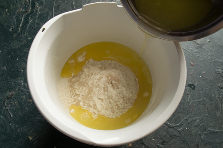 Step 3: Combining wet and dry ingredients to start the dough. The warm milk whey mixture being poured into the bowl of flour and yeast.