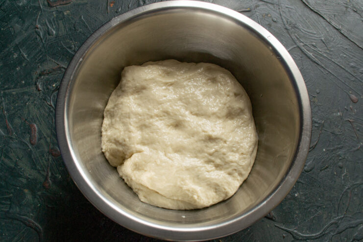 Step 5: Preparing the dough for its first proof. A ball of smooth dough in a greased bowl, covered with plastic wrap for proofing.