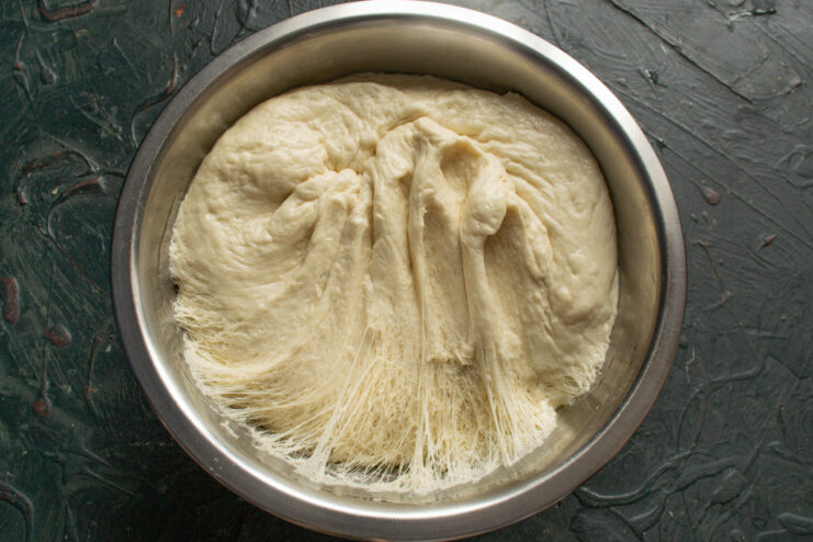Step 6: Punching down the dough after the first rise. The risen dough being punched down in a bowl before the second proof.