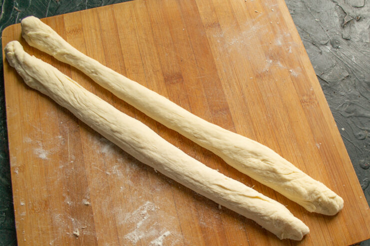 Step 8: Shaping the dough portions into long ropes. A piece of dough being rolled into a long rope on a wooden board.