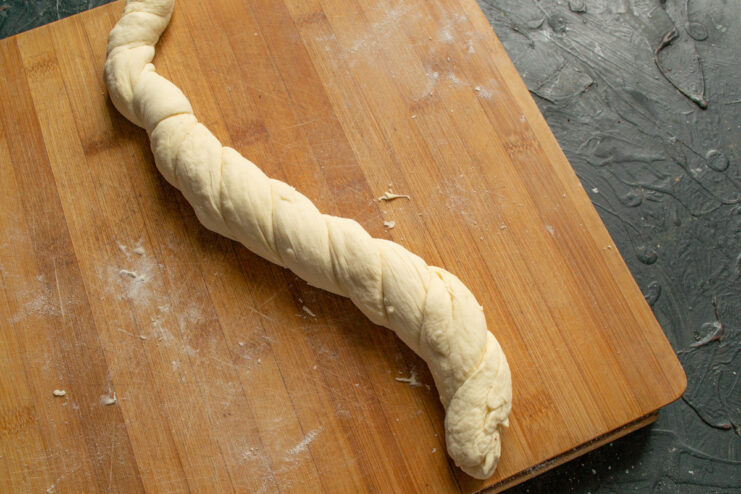 Step 9: Twisting two dough ropes together to form a braid. Two long ropes of dough being twisted together to create a braided effect.