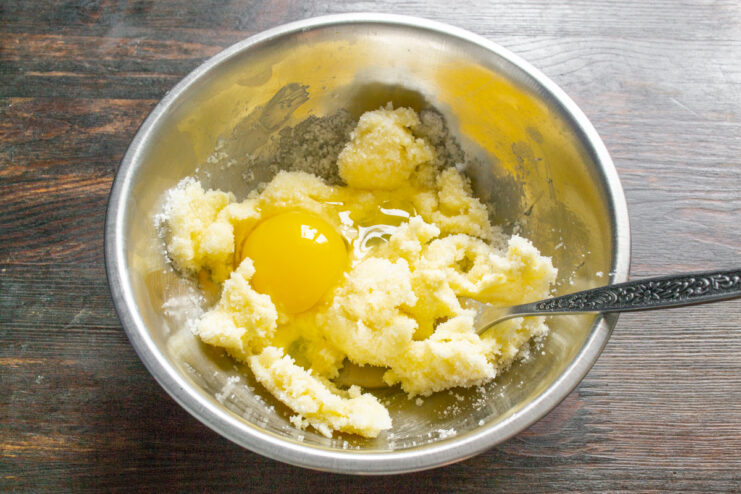 Adding an egg to the butter and sugar mixture An egg being added to the creamed butter and sugar in a bowl.
