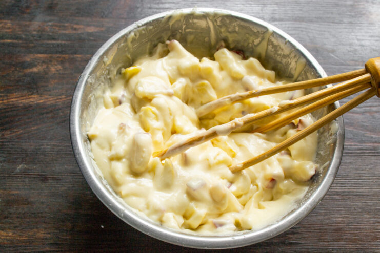 Folding diced apples into the smooth champagne batter Diced apples being folded into the cake batter in a bowl.
