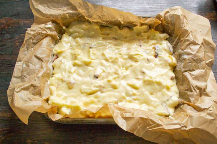 Pouring the apple pie batter into a prepared baking pan The apple and champagne batter being spread evenly in a parchment-lined baking pan.