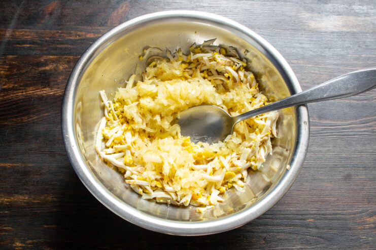 Combining Grated Eggs and Sautéed Onions Sautéed onions being added to a bowl of grated hard-boiled eggs.