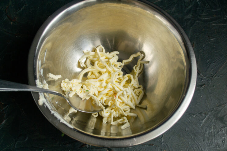 Tip: Freeze the processed cheese for 30 minutes to make it easier to grate. A hand grating a block of processed cheese on a box grater into a bowl.