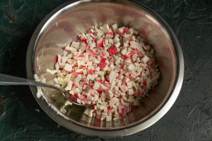 Grating frozen crab sticks is a quick way to prepare them without thawing. Crab sticks being grated on a coarse grater into a bowl with other ingredients.